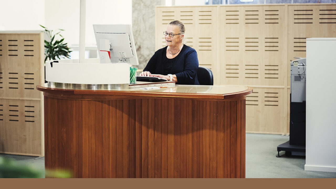 Gunilla Hillerström-Claesson sitter bakom ett skrivbord klätt i träpanel på SEB:s bankkontor vid Sergels torg. Hon skriver något på sitt tangentbord och tittar på skärmen samtidigt. Ser glad ut. Hon är klädd i blå, långärmad tröja och har glasögon. med smala mörka bågar.