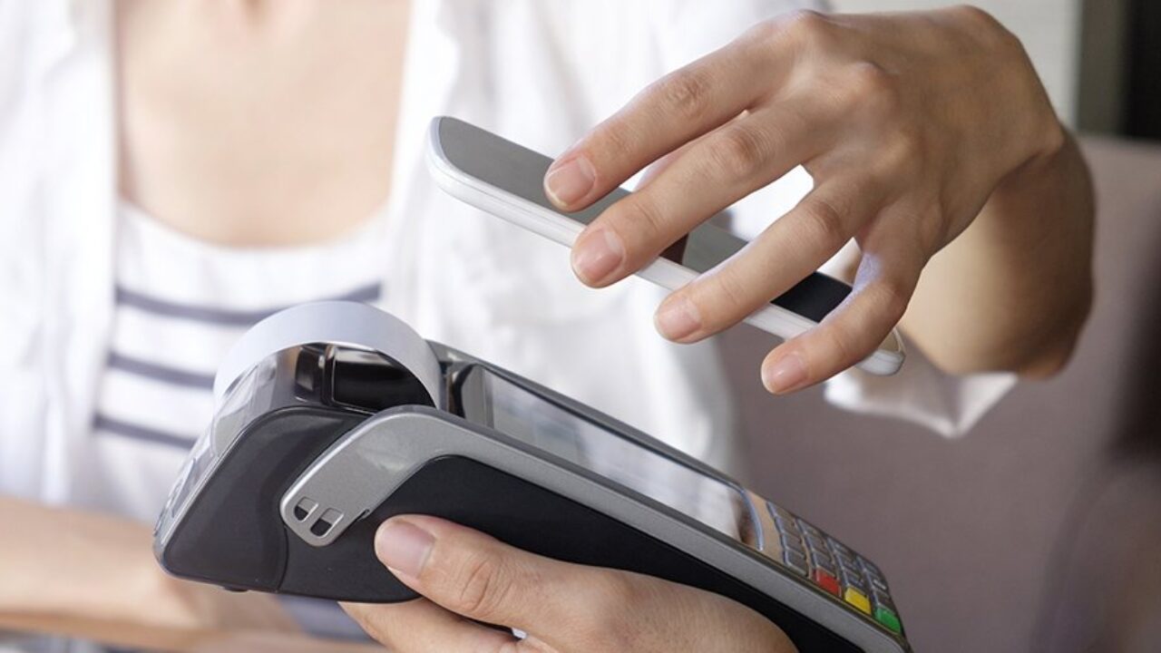 Kvinna håller mobil ovanför betaldosa.